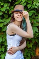 Beautiful young hipster brunete girl in hat with long green hair smiling on park background photo