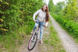 mujer joven montando en bicicleta en el parque de la ciudad de verano al aire libre. gente activa chica hipster relajarse y andar en bicicleta foto