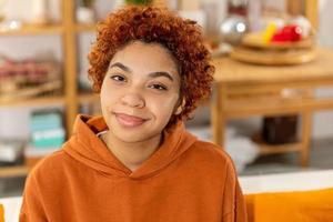 Beautiful african american girl with afro hairstyle smiling sitting on sofa at home indoor. Young african woman with curly hair smiling. Freedom happiness carefree happy people concept. photo