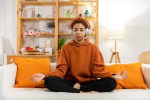 Yoga mindfulness meditation. Young healthy african girl practicing yoga at home. Woman sitting in lotus pose on yoga mat meditating smiling relaxing indoor. Girl doing breathing practice, yoga at home photo