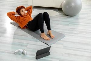 Fitness Workout training. Young healthy fit african girl doing bicycle crunch abs exercise on yoga mat on floor at home. Athletic woman in sportswear is pumping abdominals. Sport and fitness. photo