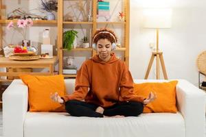 Yoga mindfulness meditation. Young healthy african girl practicing yoga at home. Woman sitting in lotus pose on yoga mat meditating smiling relaxing indoor. Girl doing breathing practice, yoga at home photo