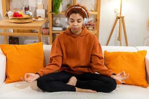 Yoga mindfulness meditation. Young healthy african girl practicing yoga at home. Woman sitting in lotus pose on yoga mat meditating smiling relaxing indoor. Girl doing breathing practice, yoga at home photo