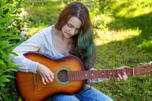 joven mujer sentado en césped y jugando guitarra foto