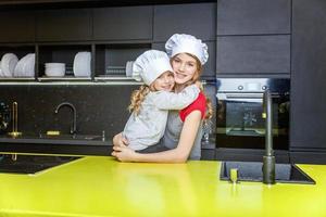 Two girls with chef hat hugging and having fun in kitchen photo