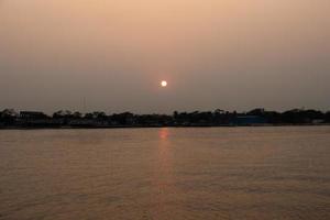 hermosa puesta de sol y naturaleza ver a oscuridad tiempo. puesta de sol ver desde el orilla del río. hermosa naturaleza con amarillo cielo y árbol horizonte. calma río ver a crepúsculo. el natural paisaje de un río y puesta de sol foto