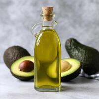 A bottle of olive oil with avocado on the table behind it photo