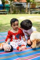 dos contento Niños en sociedad parque, contento asiático hermanos quien son sonriente felizmente juntos. hermanos jugar al aire libre en verano, mejor amigos. niñito bebé chico jugando con su contento hermano en el jardín foto