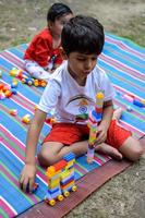 dos contento Niños en sociedad parque, contento asiático hermanos quien son sonriente felizmente juntos. hermanos jugar al aire libre en verano, mejor amigos. niñito bebé chico jugando con su contento hermano en el jardín foto