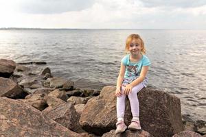 A little girl is sitting on the rocks by the sea. Gulf of Finland. Summertime photo