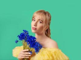 Beautiful young blonde caucasian woman in yellow dress with blue cornflower on green background. Fashion, Ukraine, flowers, style concept photo