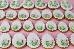 A pink table with decorated Easter cookies and decorated eggs. photo