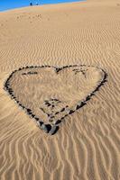heart symbol of love arranged from gray stone on golden sand on a golden dune photo