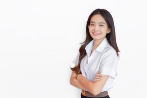 Portrait of adult Thai student. Cute Asian young woman student in uniform is smiling and looking at camera with her arms crossed confidently on white background in the university photo