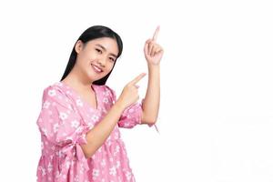 Asian cute woman with black long hair in pink shirt shows hand point up to present something isolated on a white background. photo