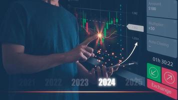 Businessman or trader is using smartphone and virtual hologram stock, invest in trading, planning analyze indicator and strategy for year 2024 buy and sell, Stock market, Business growth concept. photo