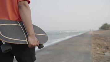 homem caminhando com surfar skate perto a mar video
