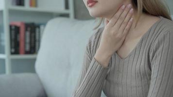 Aisa woman put her hand on her neck due to a sore throat. female tonsillitis causes a inflammation. treated by taking water, taking antibiotics, consult a doctor, virus, corona virus, Influenza, flu video