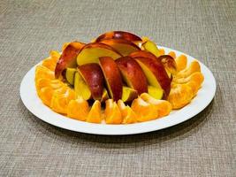 Peeled tangerines sliced and red and yellow apples cut into slices on a white plate. Healthy food concept. photo