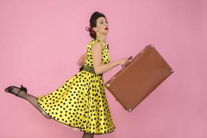 Retro girl with an old suitcase on a pink background. photo