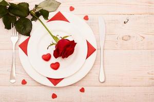 Top view of tableware of round and heart shaped empty plate, metal knife and fork served on white wooden table with glowing candle and gift box prepared for celebration of saint valentine day photo
