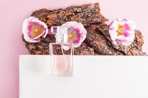 a transparent bottle of women's perfume lies on part of the white podium and bark of a tree with spring flowers. presentation of spring fragrance. photo