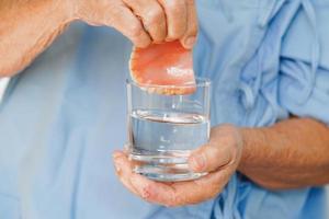 Asian senior woman patient holding teeth denture in her hand for chew food. photo