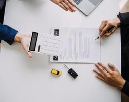 Closeup of Asian female signing car insurance document or lease paper contract or agreement. Buying or selling new or used vehicle with car keys on table. photo