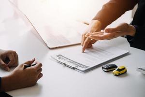 Closeup of Asian female signing car insurance document or lease paper contract or agreement. Buying or selling new or used vehicle with car keys on table. photo