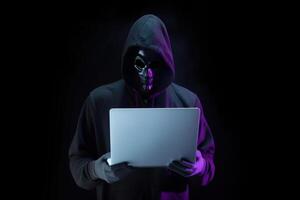 a hacker in a hoodie using a laptop computer isolated on dark background with neon light. photo