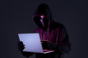 a hacker in a hoodie using a laptop computer isolated on dark background with neon light. photo