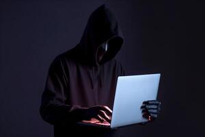 a hacker in a hoodie using a laptop computer isolated on dark background with neon light. photo