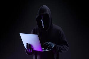 a hacker in a hoodie using a laptop computer isolated on dark background with neon light. photo