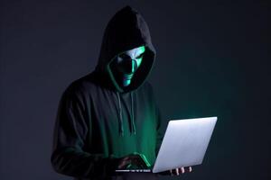 a hacker in a hoodie using a laptop computer isolated on dark background with neon light. photo
