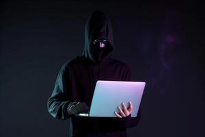 a hacker in a hoodie using a laptop computer isolated on dark background with neon light. photo