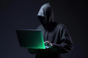 a hacker in a hoodie using a laptop computer isolated on dark background with neon light. photo