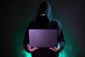 a hacker in a hoodie using a laptop computer isolated on dark background with neon light. photo