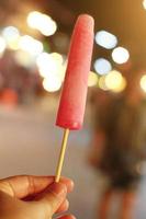 Hand holding Thai homemade Ice cream or ice freezer pop in bokeh light at night market and street food photo
