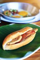 Baguette bread sandwich with cheese, ham on fresh Green banana leaf and Indochina pan-fried egg with toppings with on wooden table in homemade Thai style photo
