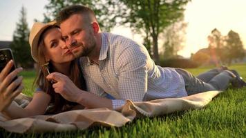 Paar im Liebe Lügen auf ein Plaid im das Park und Herstellung selbst Foto beim Sonnenuntergang video