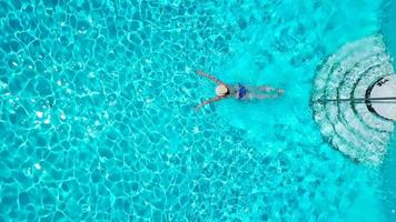 Visualizza a partire dal il superiore come un' donna nel un' blu costume da bagno nuotate nel il piscina video