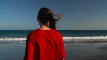 content Jeune femme dans rouge robe en marchant à le l'eau sur le océan plage à le coucher du soleil. concept de insouciant moderne la vie video
