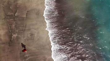 Top view of a woman in red dress walking barefoot along wet sand ocean beach video