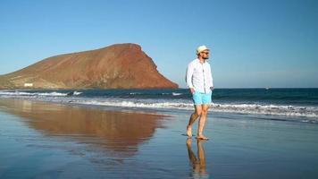 contento hombre caminando a lo largo el Oceano playa a puesta de sol. concepto de despreocupado moderno vida. tenerife, canario islas, España video