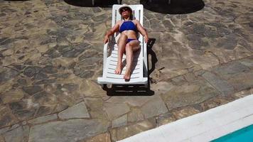 Visualizza a partire dal il superiore come un' donna nel un' blu costume da bagno prende il sole su un' lettino, prende su, va per il piscina e nuotate nel il piscina video