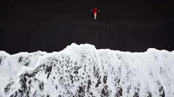 Aerial view of a girl in a red dress sitting on the beach with black sand. Tenerife, Canary Islands, Spain video