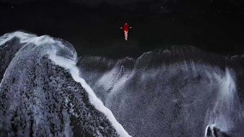 aereo Visualizza di un' ragazza nel un' rosso vestito seduta su il spiaggia con nero sabbia. tenerife, canarino isole, Spagna video