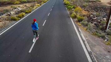 aereo Visualizza di il donna corre lungo il abbandonato asfalto strada a tramonto, indietro Visualizza. montagne su il sfondo video