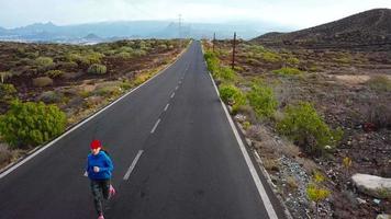 aereo Visualizza di il donna corre lungo il abbandonato asfalto strada a tramonto, indietro Visualizza. montagne su il sfondo video