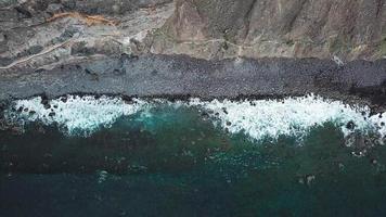 topo Visão do uma deserta Preto vulcânico de praia. costa do a ilha do tenerife. aéreo zangão cenas do mar ondas alcançando video